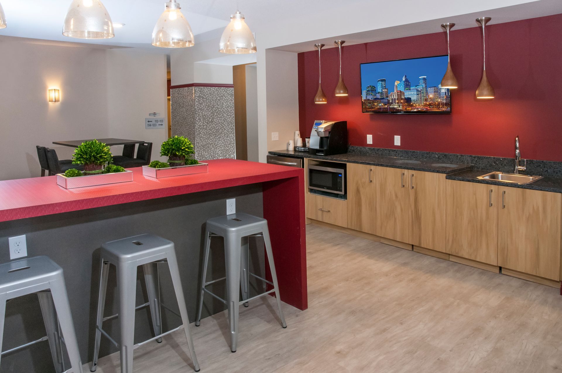 Kitchen area with red countertop, stools, cabinetry, TV, and lighting.