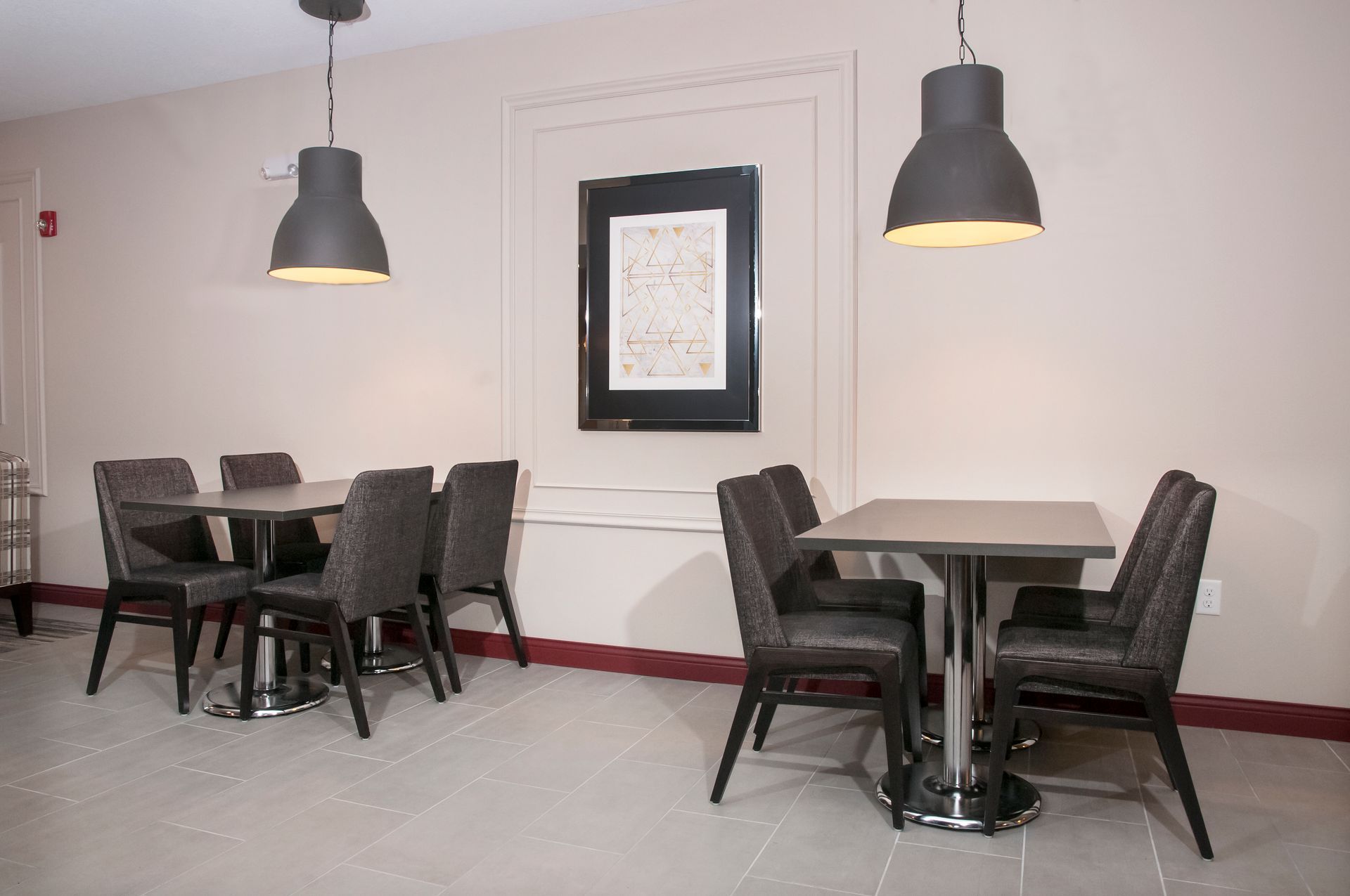Small dining area with tables, chairs, pendant lights, and artwork on the wall.