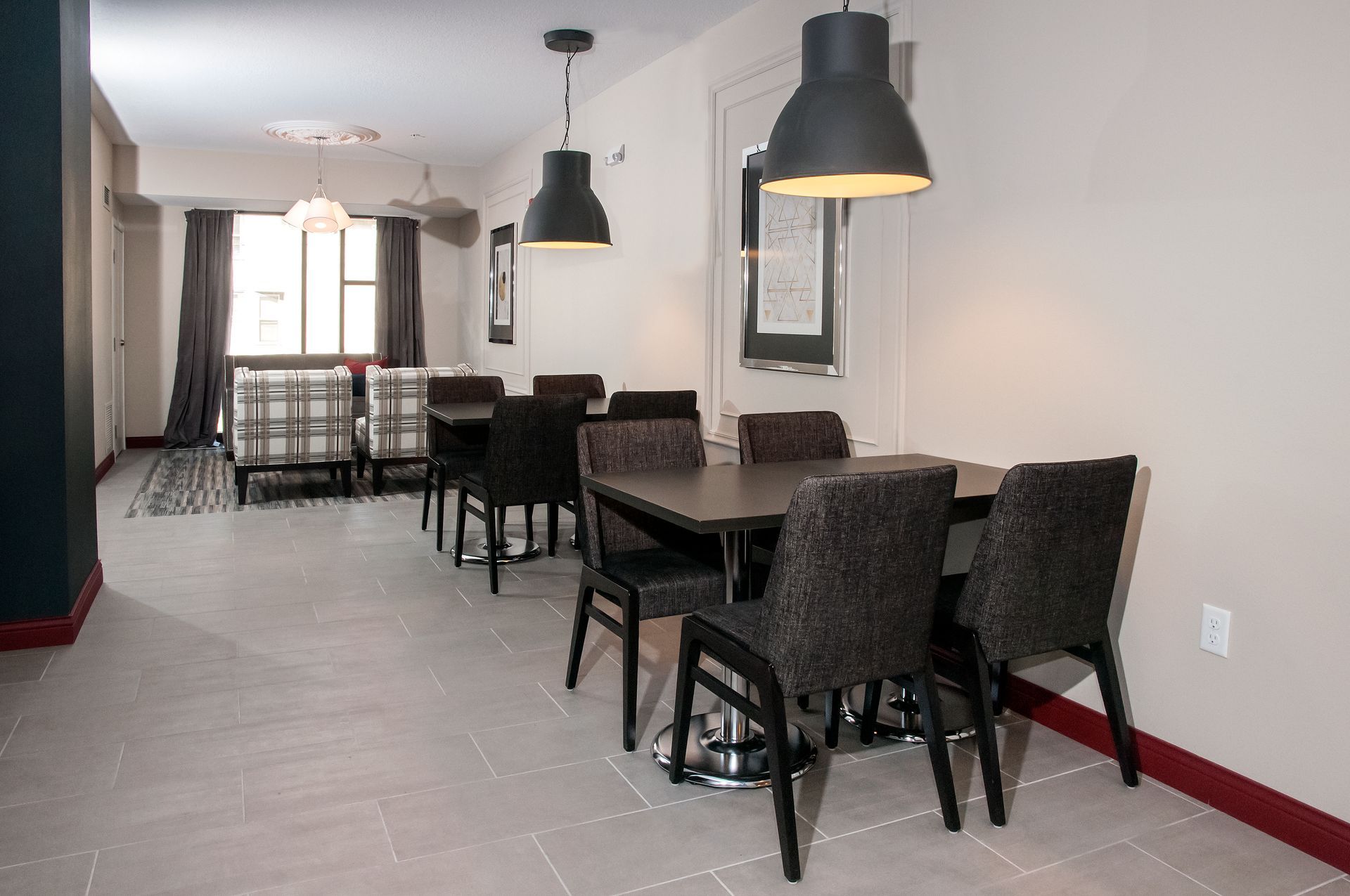 Dining area with tables, chairs, pendant lights, and a window with dark curtains.