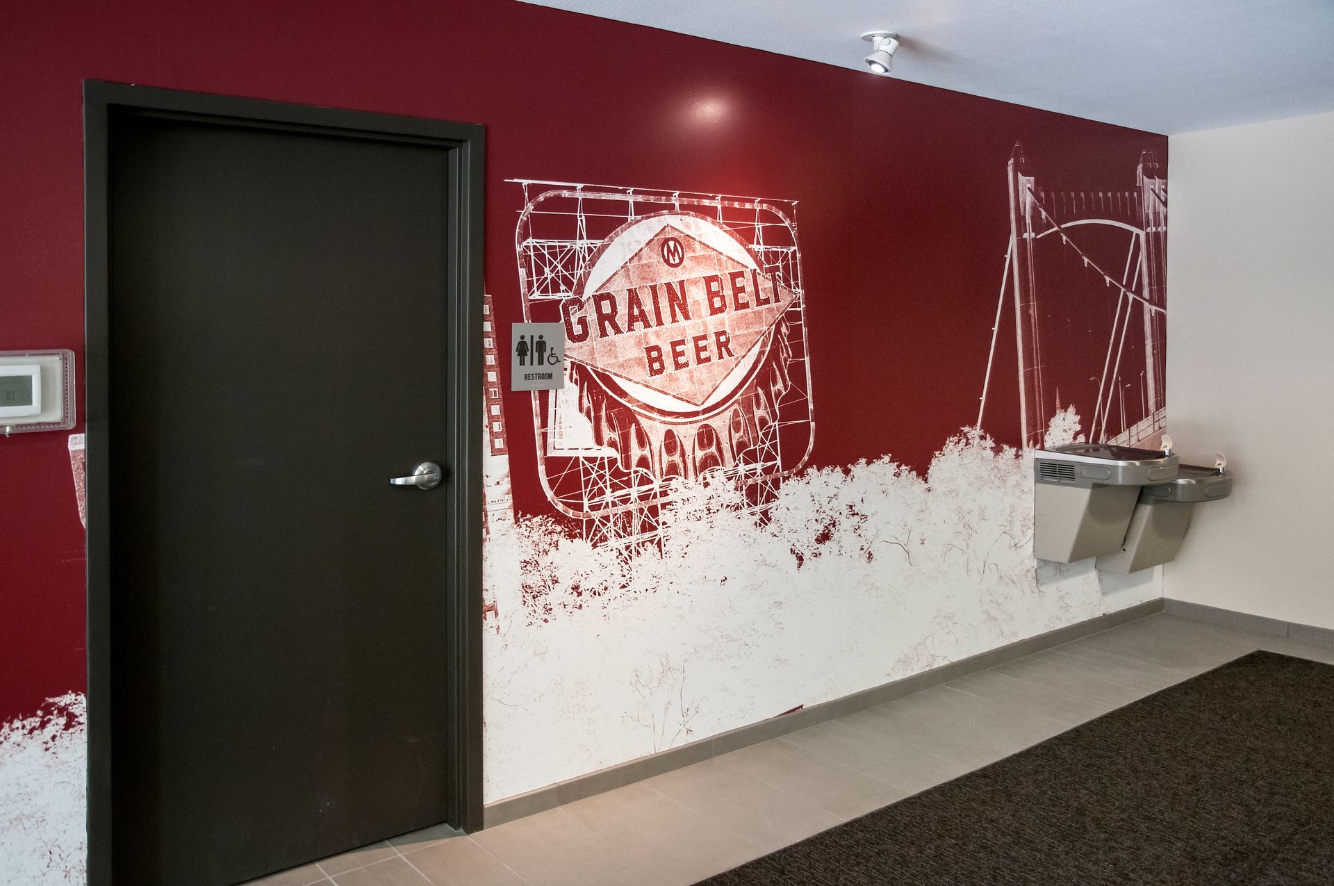 Red wall with white graphics, door, water fountain in a hallway.