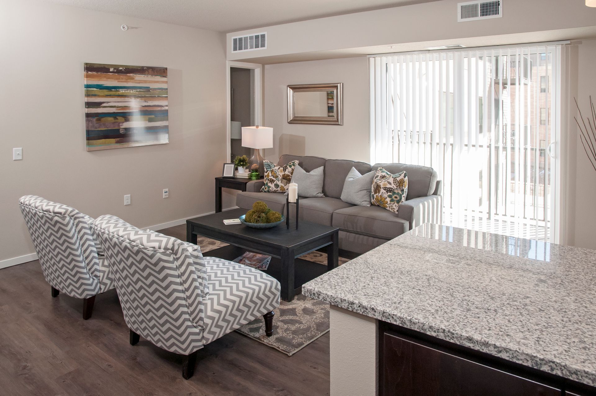 Living room with gray sofa, patterned armchairs, coffee table, and sliding glass door.