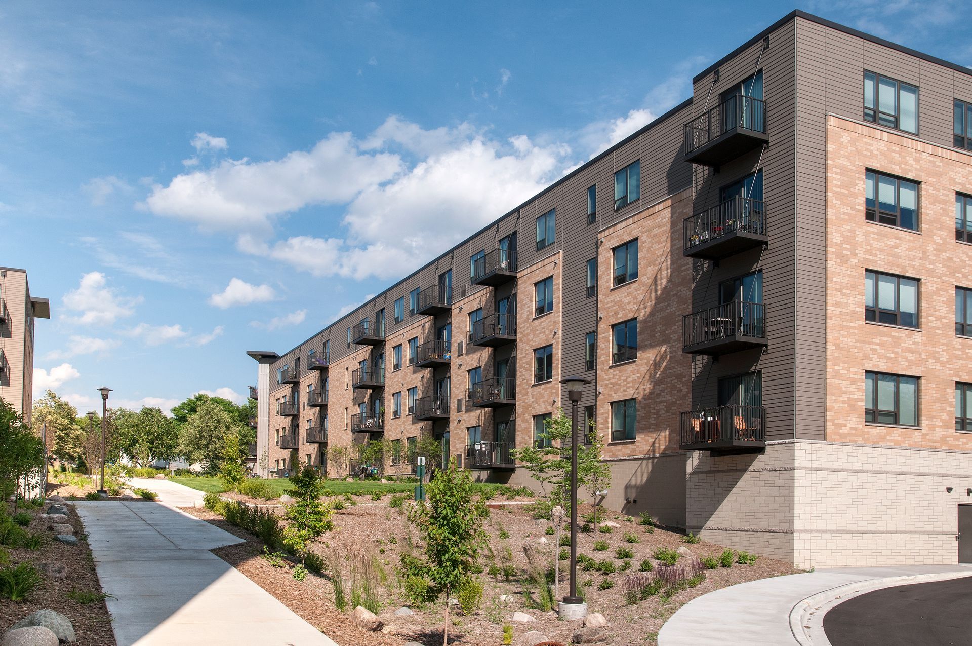 Multi-story brick building with balconies and a sloping sidewalk on a sunny day.