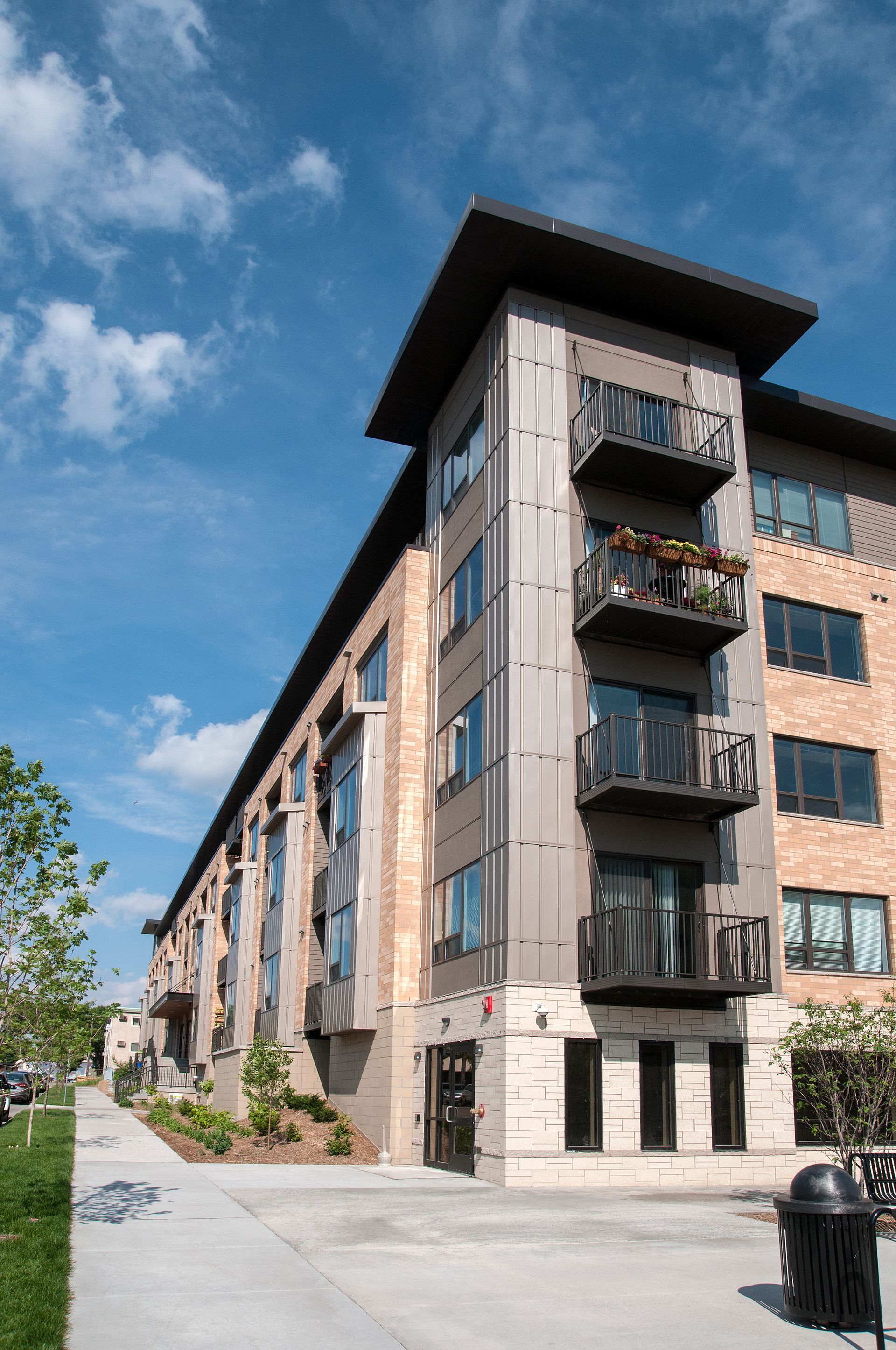 Multi-story modern building with balconies, brick, and metal facade under a blue sky.