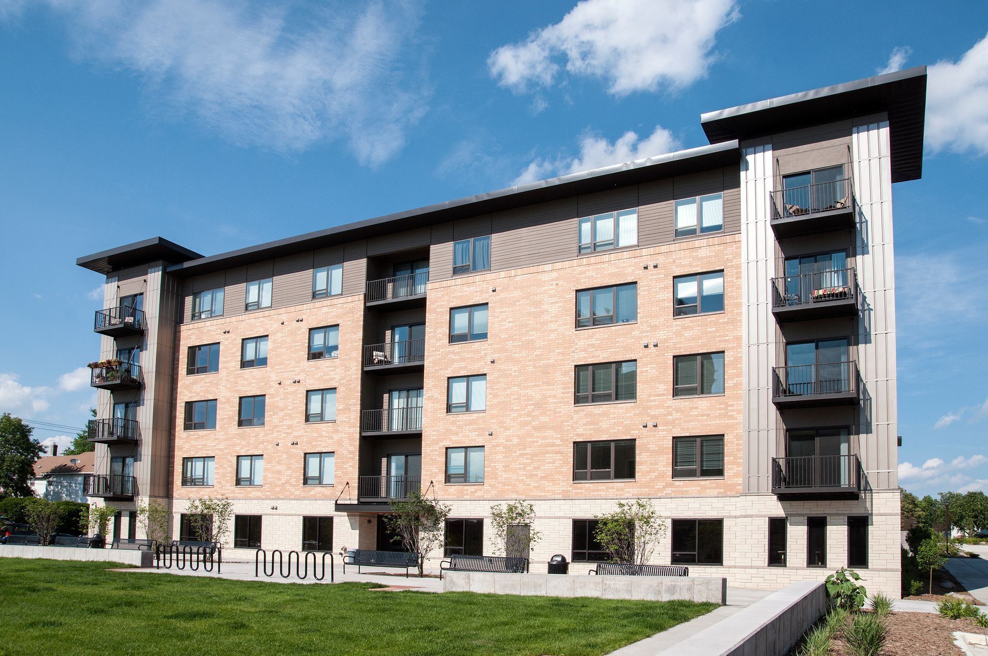Multi-story brick apartment building with balconies, under a blue sky.
