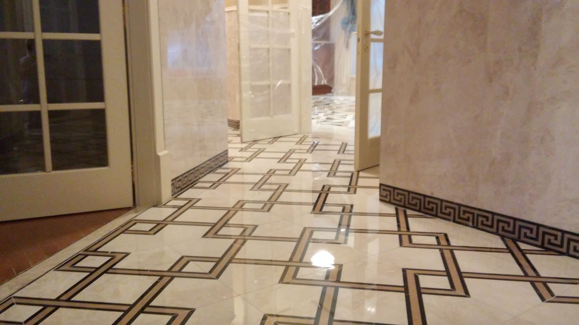 Marble hallway with patterned tile floor, open doorways, and warm wall lighting