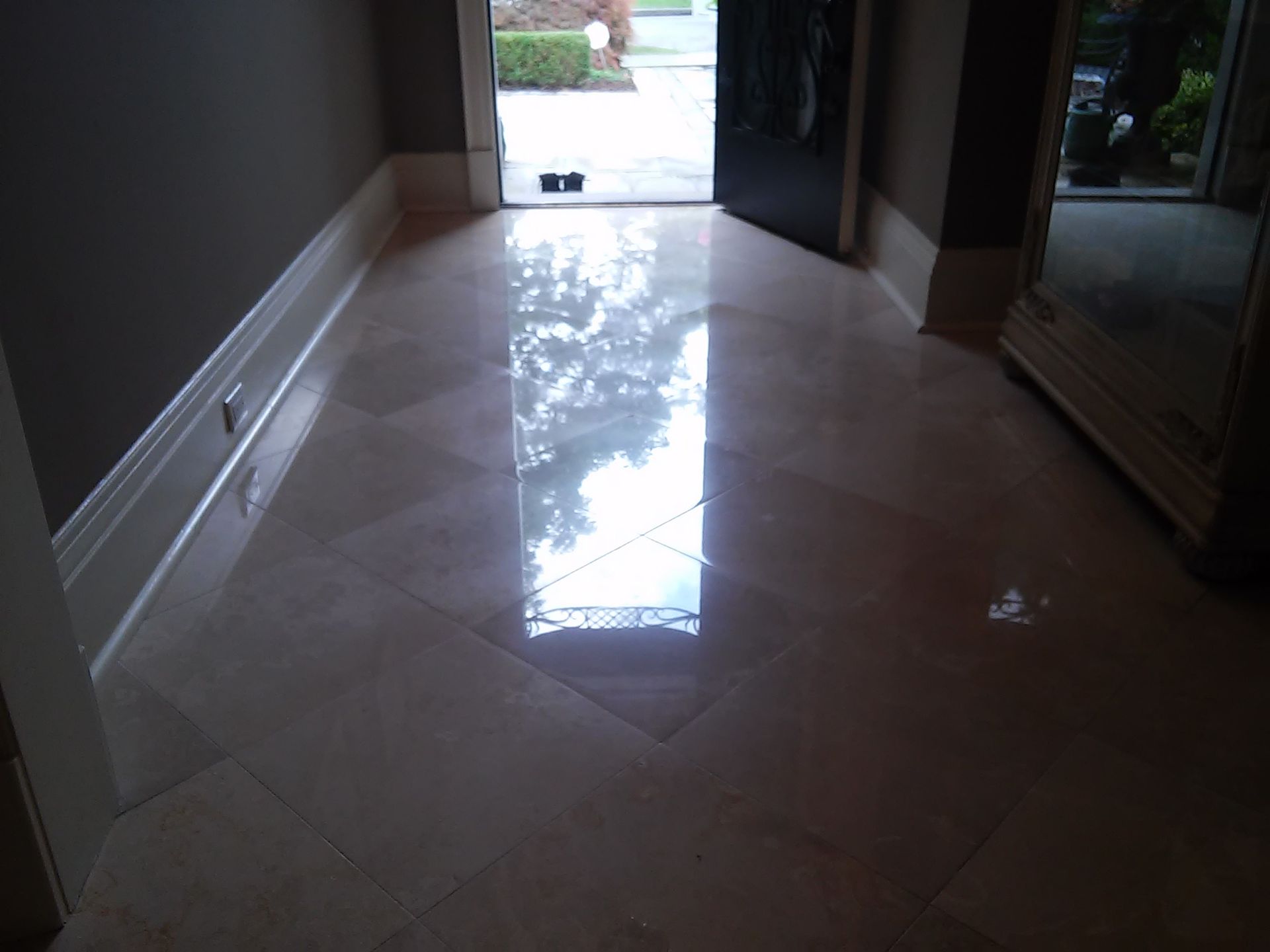 Polished light-colored stone floor in an entryway reflecting bright sunlight from an open doorway.