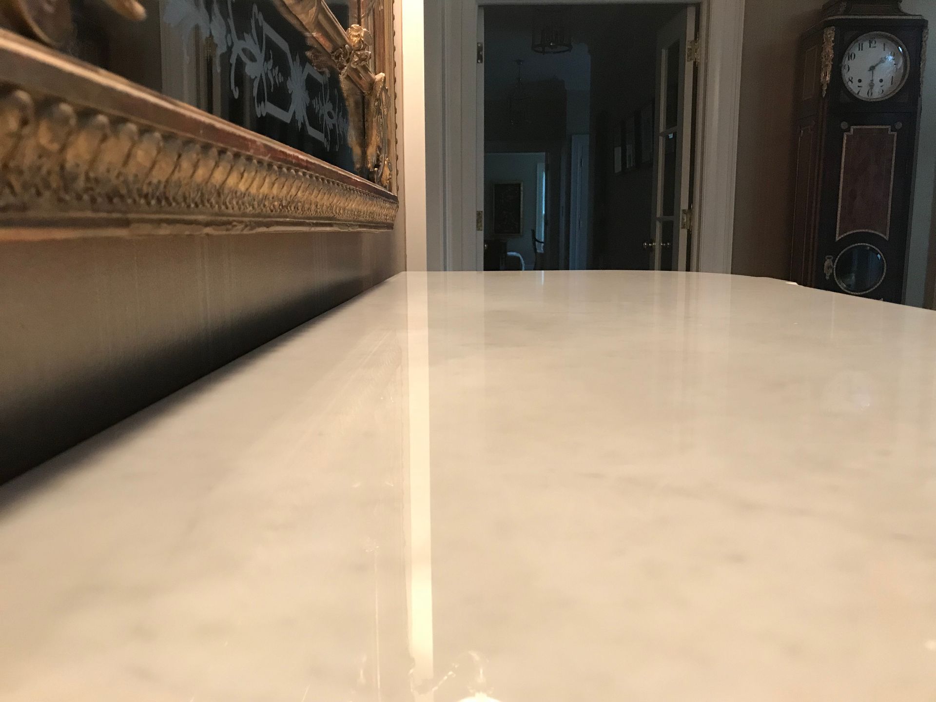 White marble surface with a reflection, hallway in the background, and antique clock.