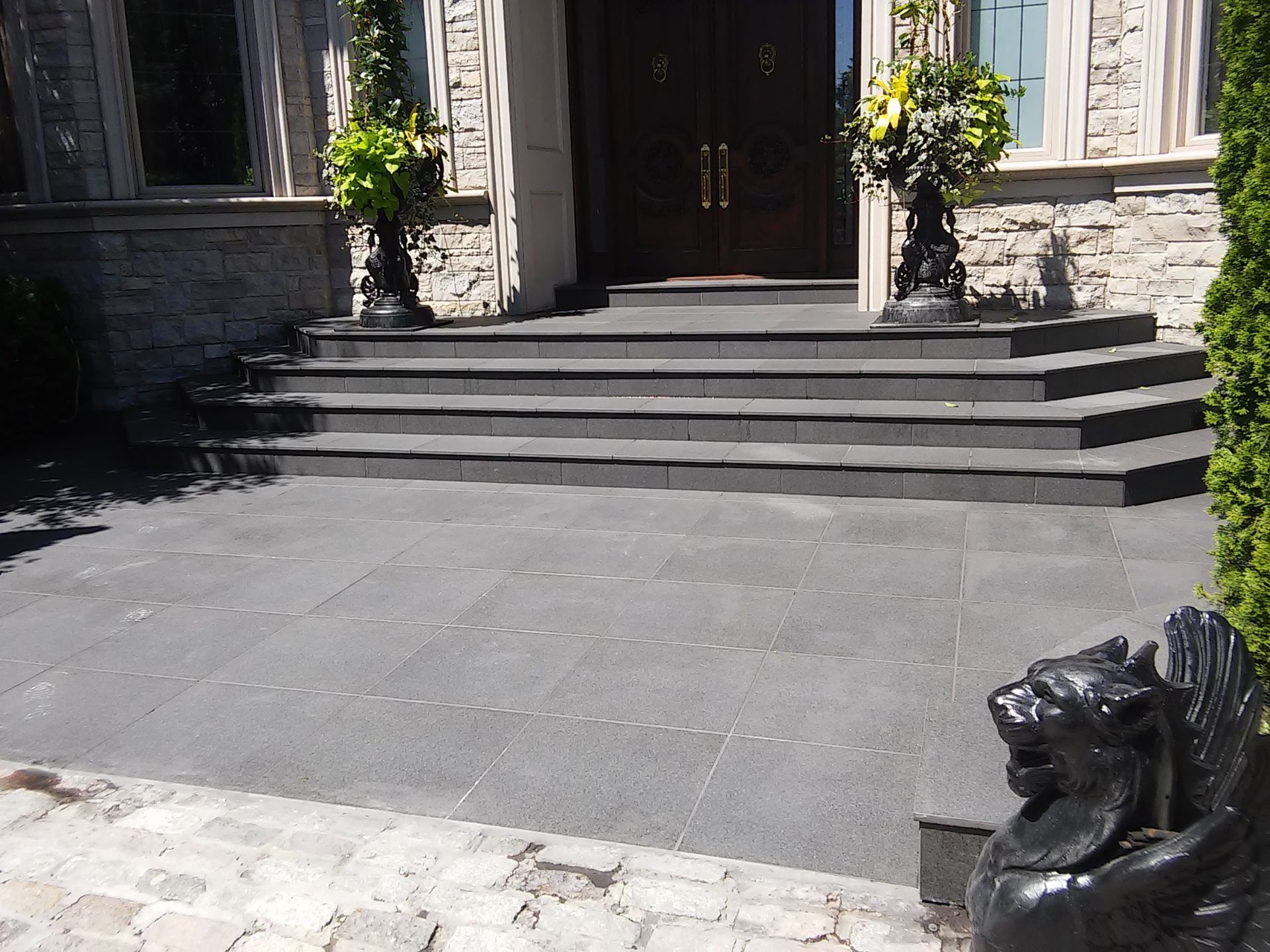 Stone house entrance with wide front steps, gray patio, and two potted plants by the doorway