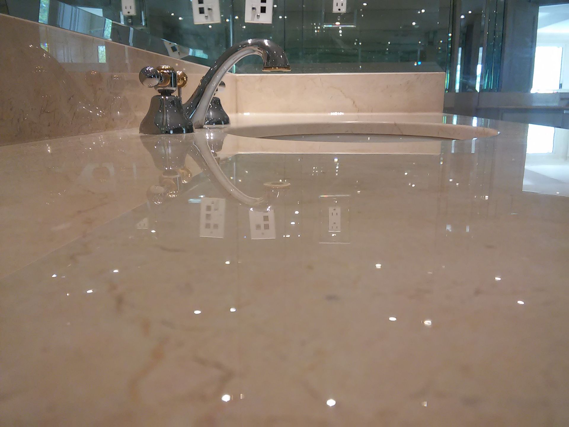 Shiny beige marble countertop with a faucet and reflection of electrical outlets.