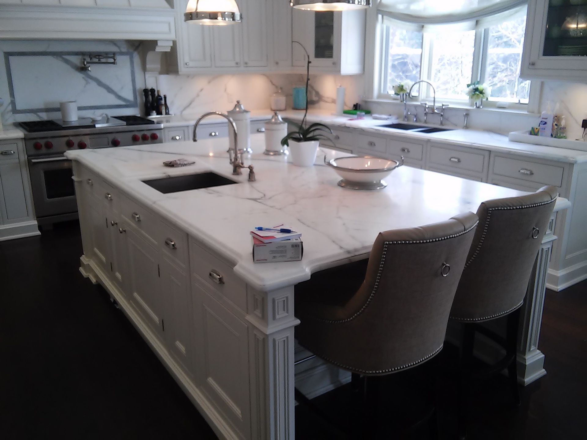 Elegant white kitchen with marble countertops, island with two chairs, dark wood floors.