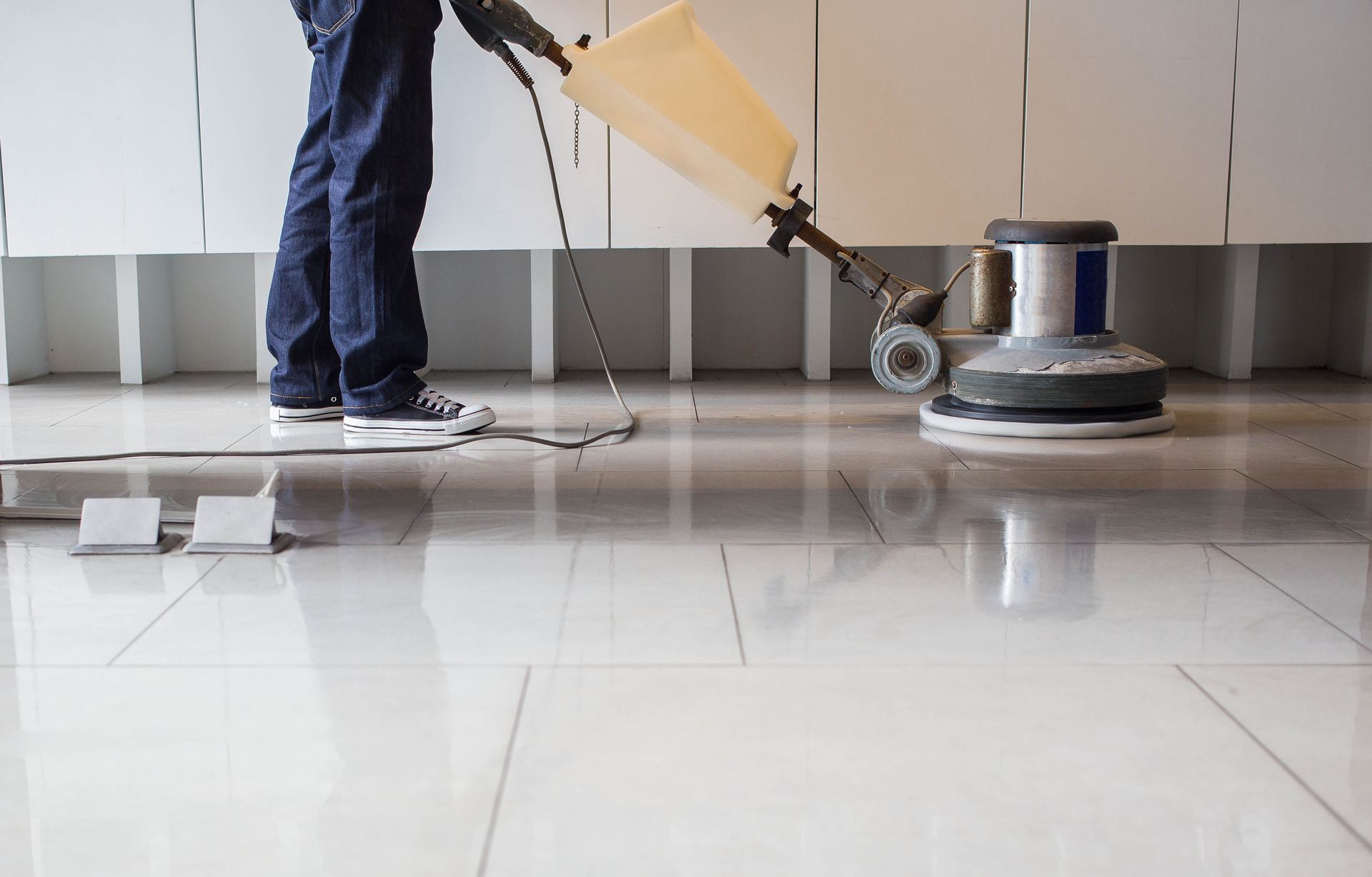 Person polishing a shiny white tile floor with a buffing machine.