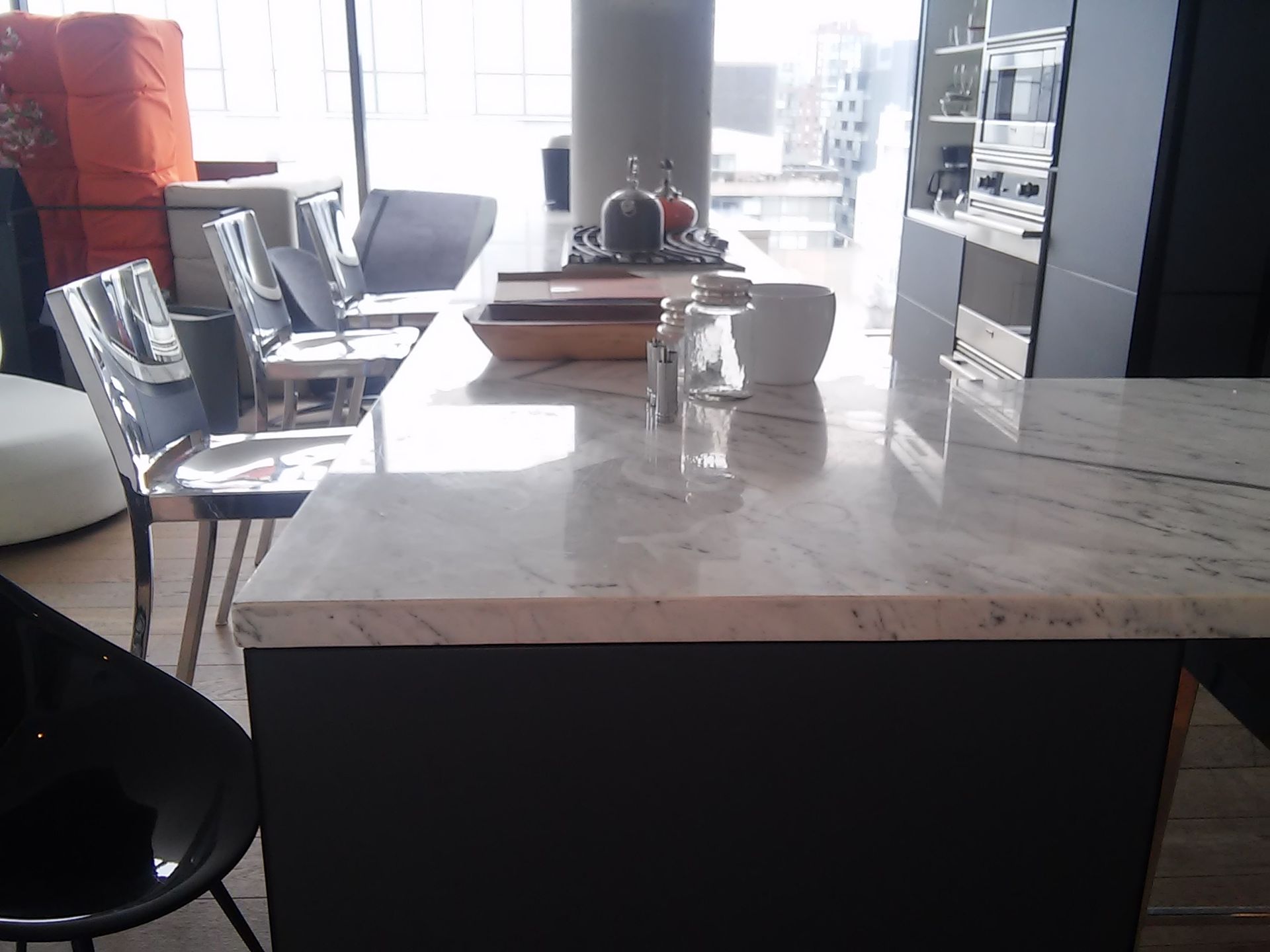 A kitchen island with a marble countertop, clear chairs, and a modern setting.