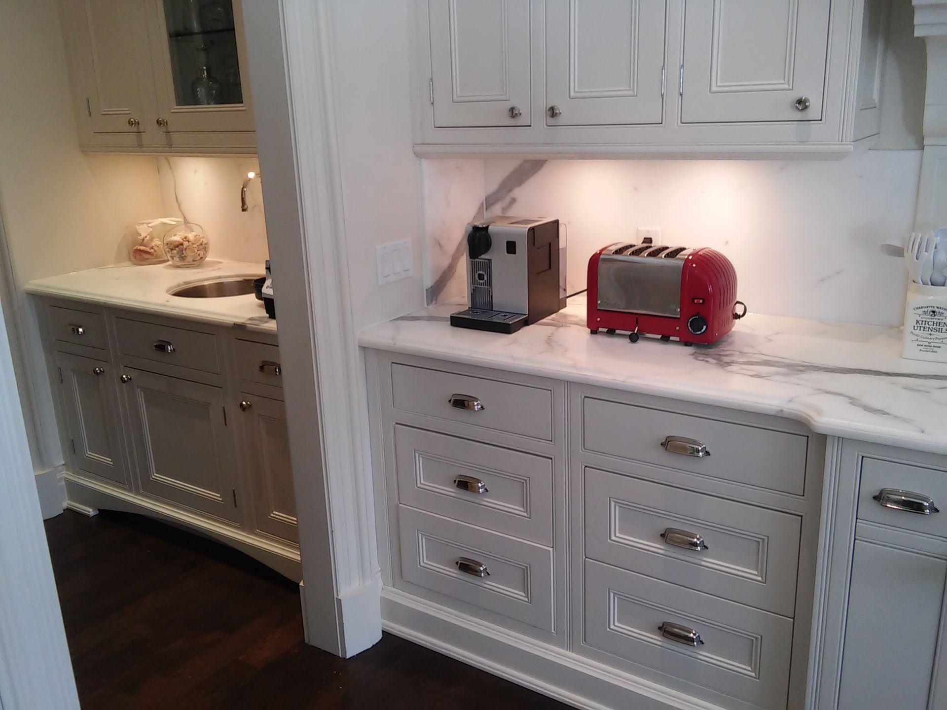 White cabinets and countertop in a kitchen; a coffee maker and red toaster sit on the counter.