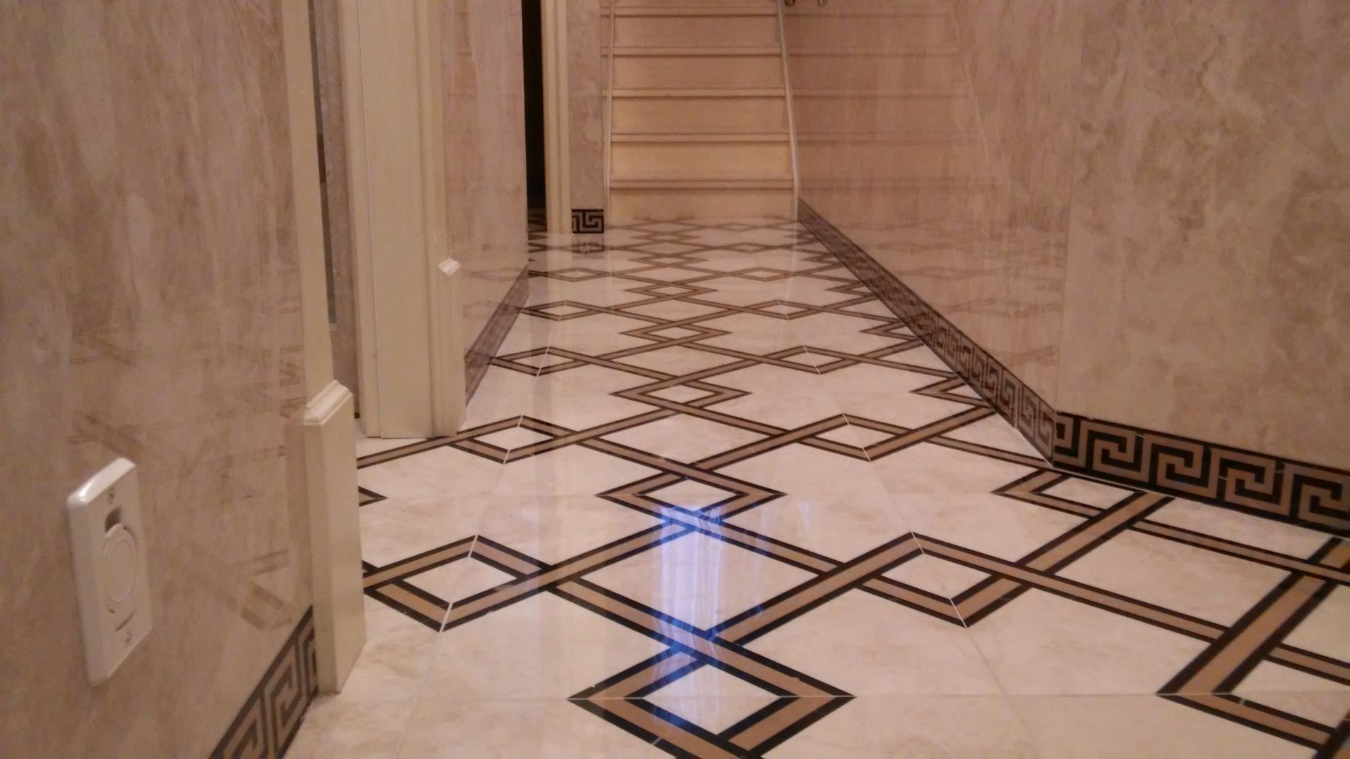 Hallway with patterned tile floor, marble walls, and a door on the left.