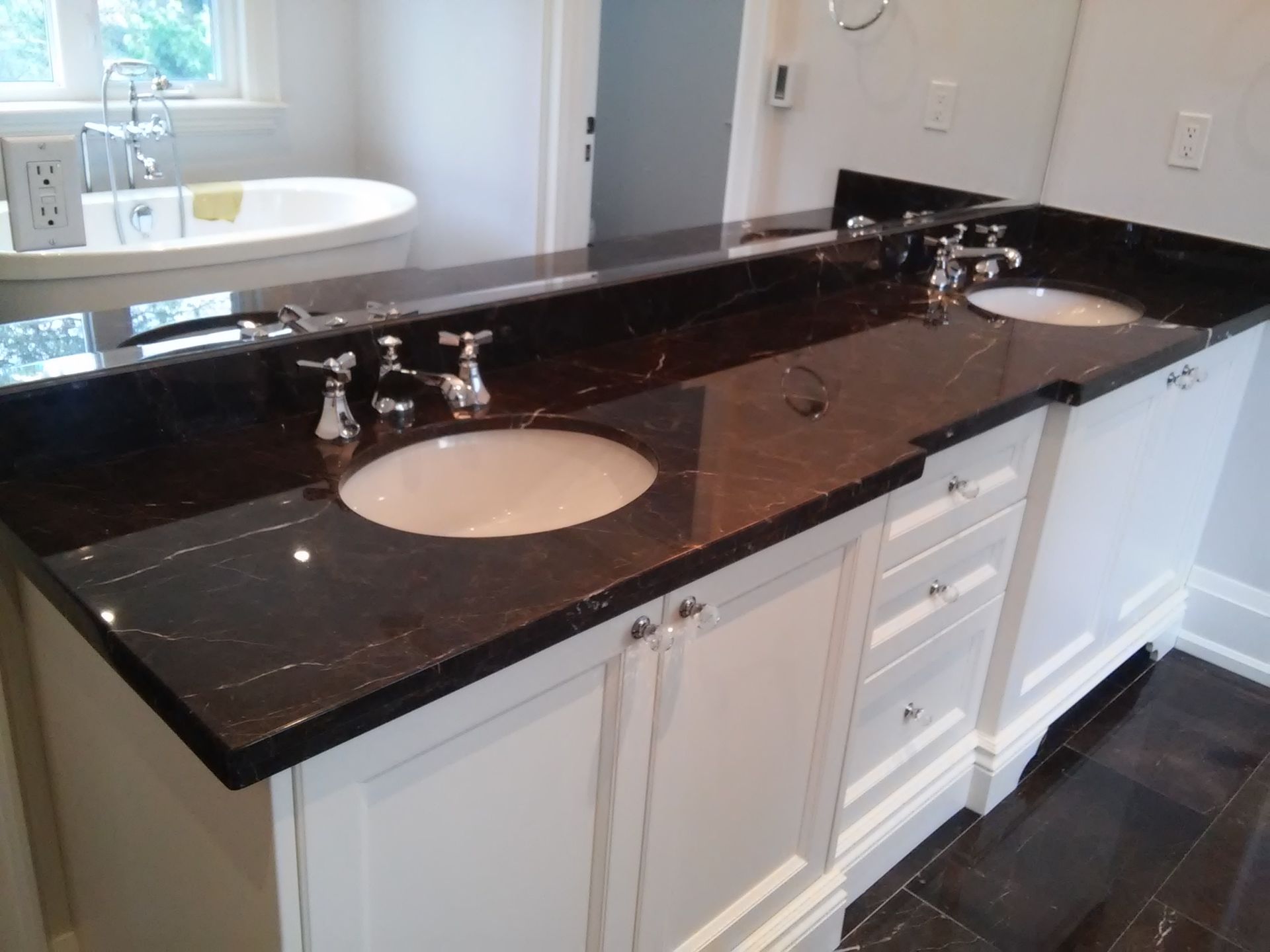 Bathroom with white cabinets, dark countertop, and two sinks.