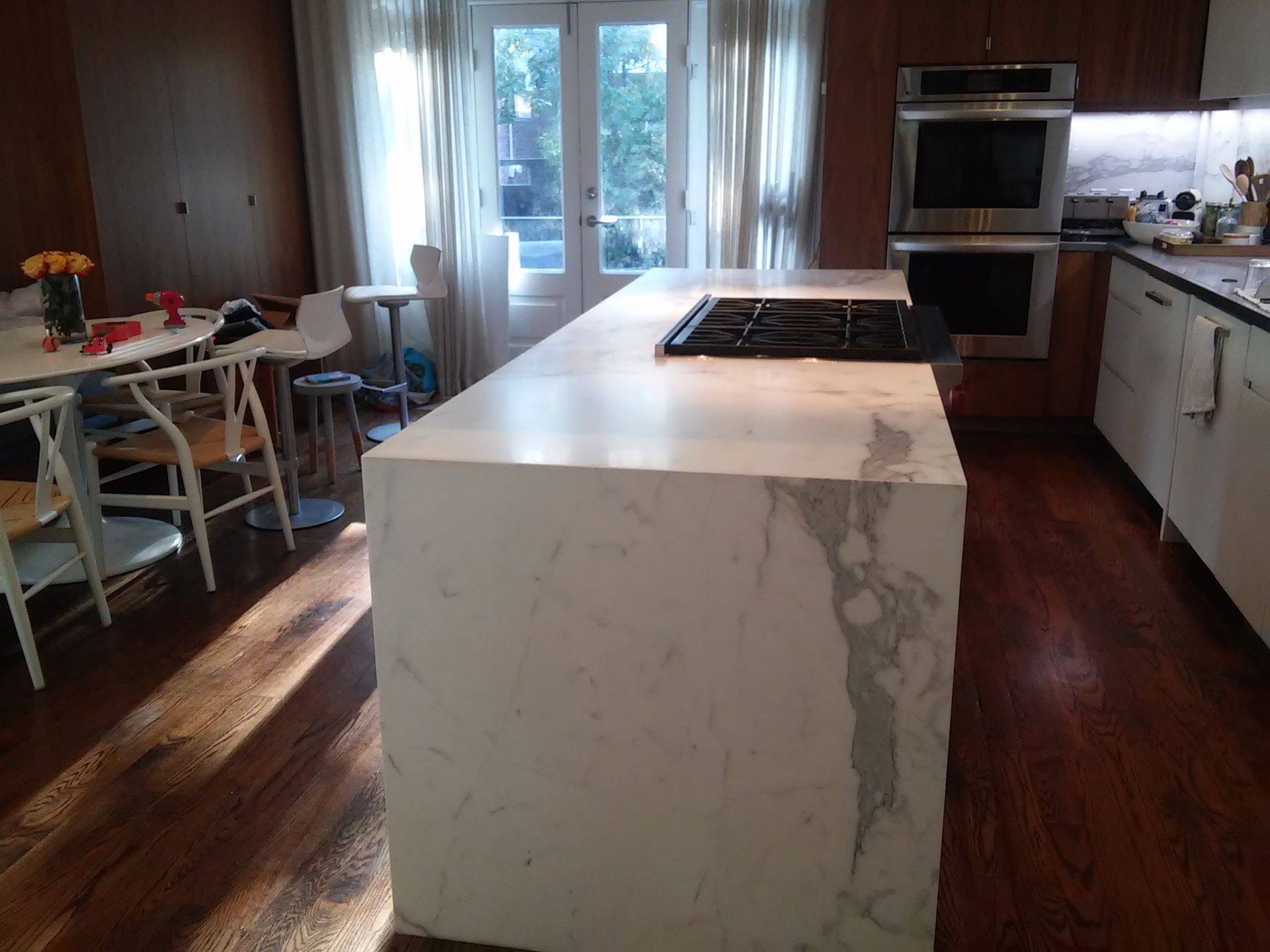 Kitchen with white marble island and cooktop. Dark wood floors, cabinets, and dining table.
