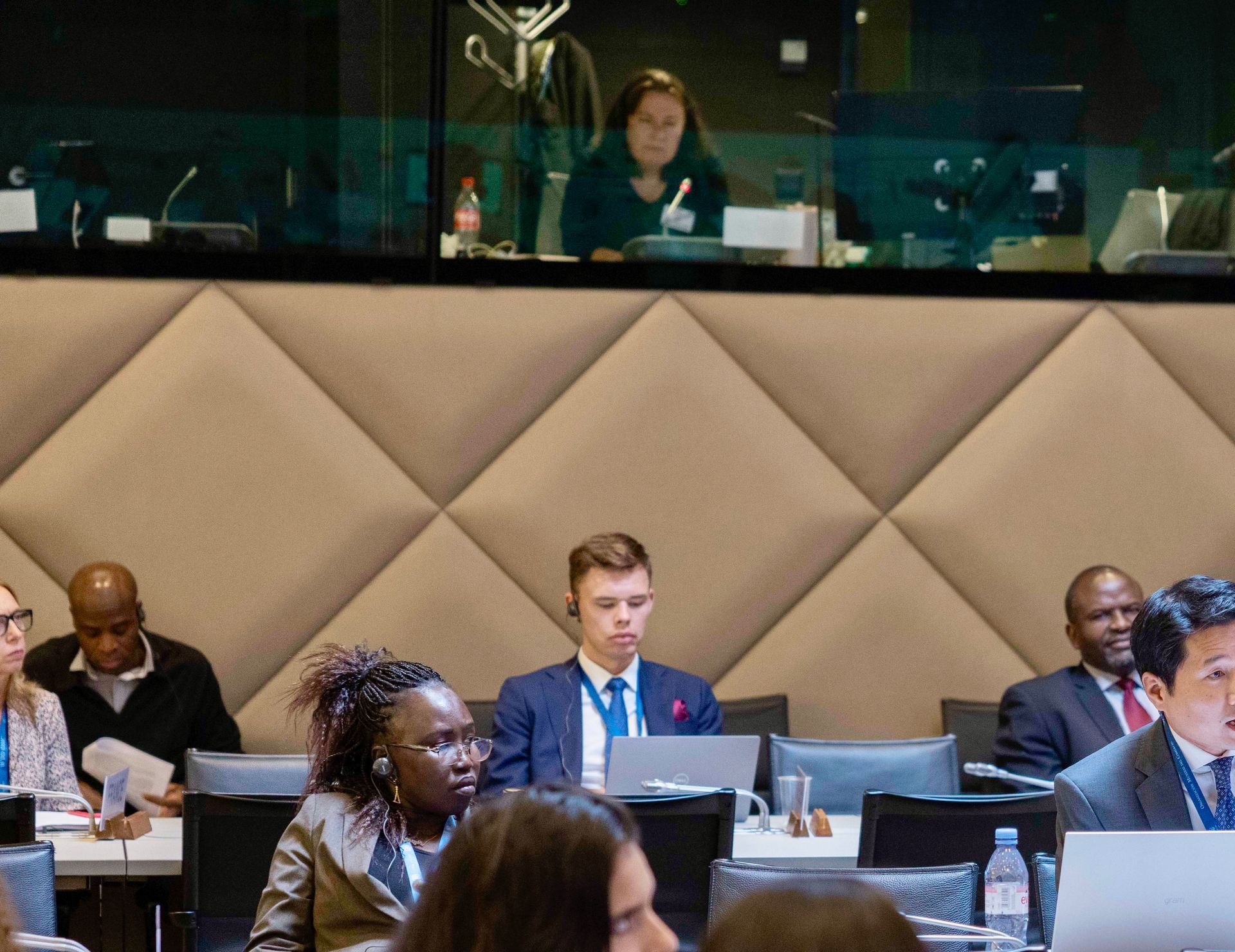 Conference attendees at a table, some using laptops. A person in a booth looks on.