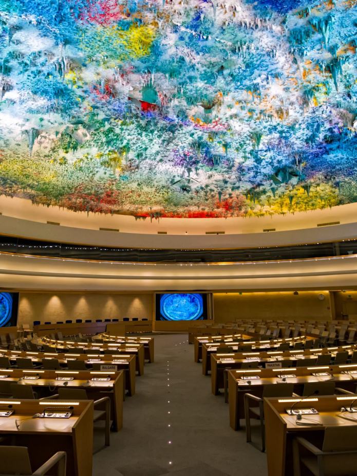 Audience chamber with colorful ceiling art, tables, and screens; interior shot.