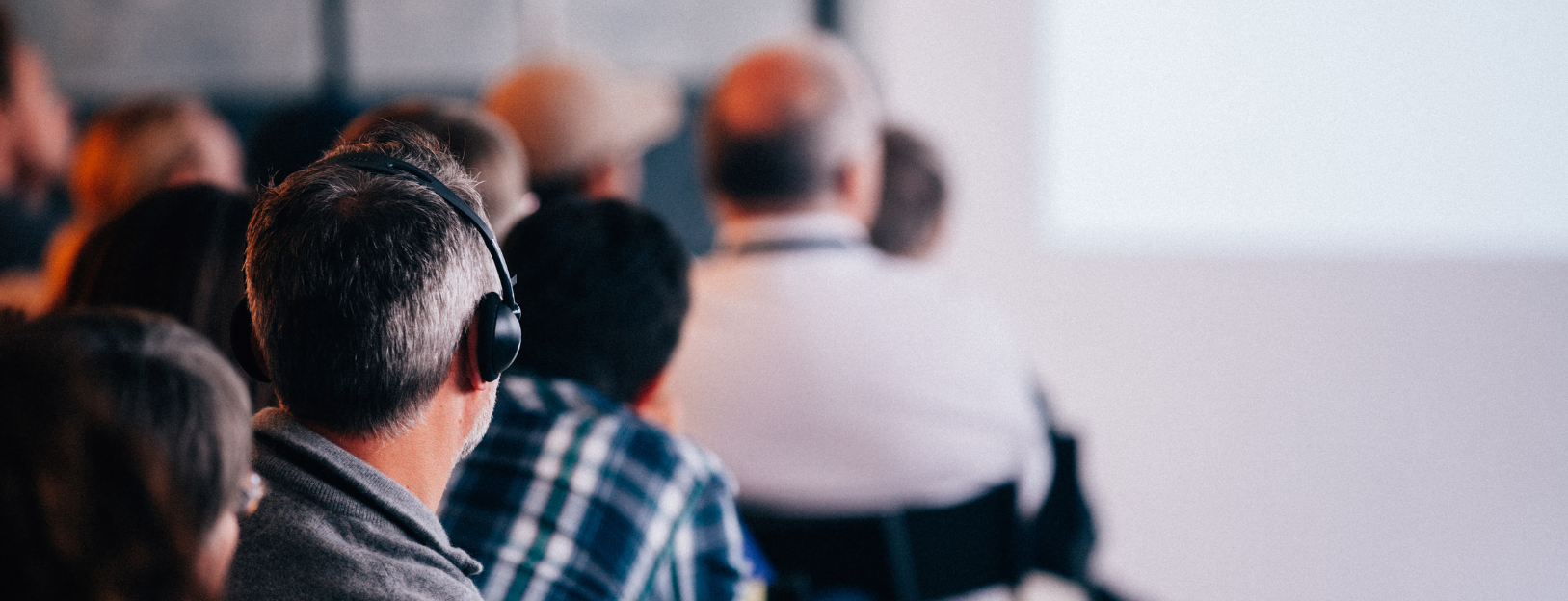 Audience members listen attentively, some wearing headphones, at a presentation.