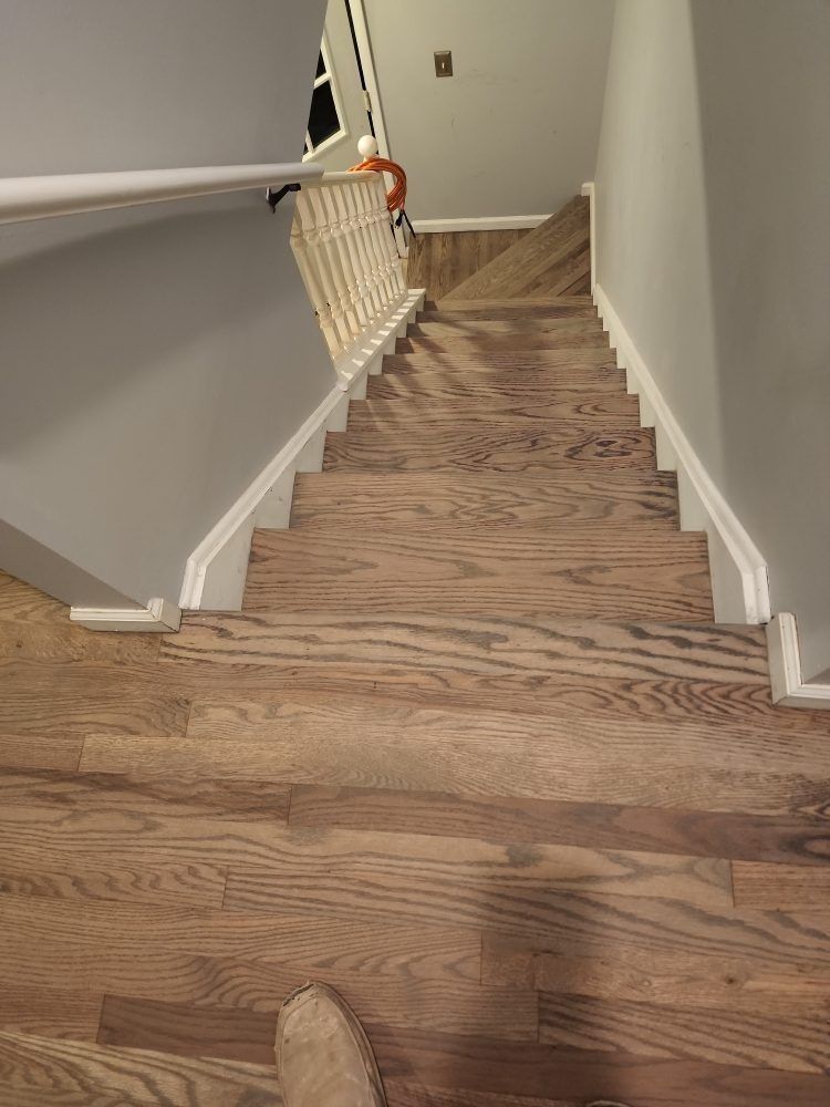 Narrow wooden staircase with white railing descending into a hallway with beige walls