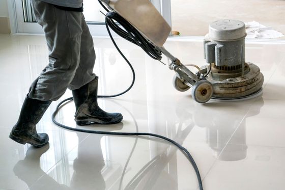 Person in boots using a floor polisher on shiny white tiles.