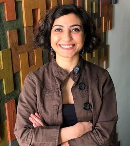 A woman in a brown jacket is smiling with her arms crossed