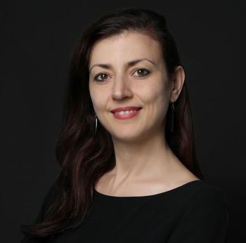 The woman is wearing a black shirt and earrings and is smiling for the camera.
