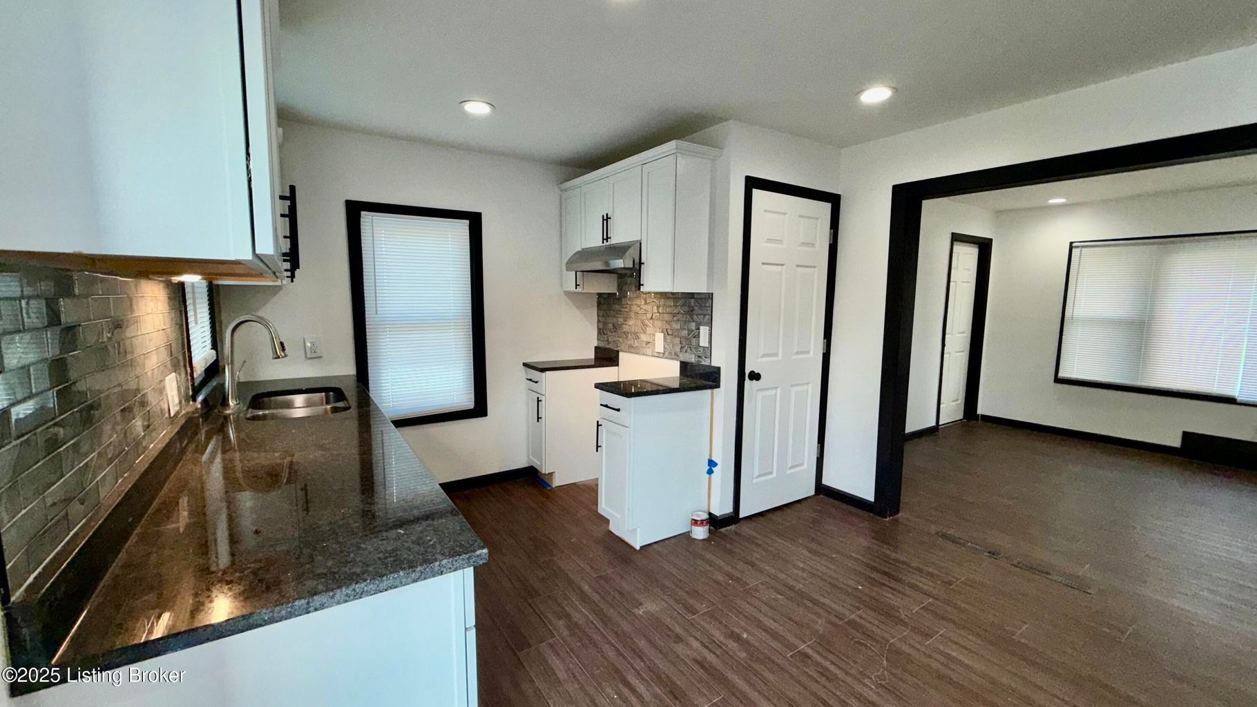 Kitchen with white cabinets, dark countertops, dark trim, and dark wood floors.