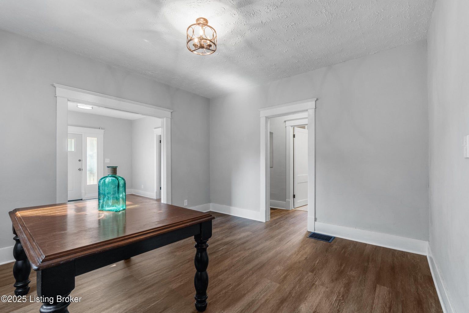 A dining room with gray walls, wood floors, a dark wood table with a blue glass vase, and a ceiling light fixture.