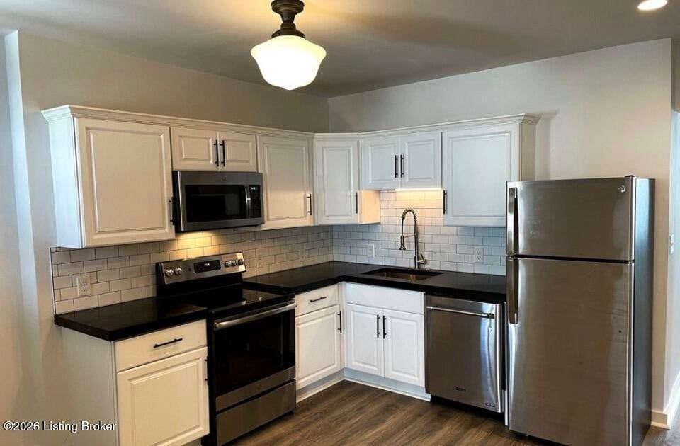 Modern kitchen with white cabinets, black countertops, stainless steel fridge, and stove under warm lighting