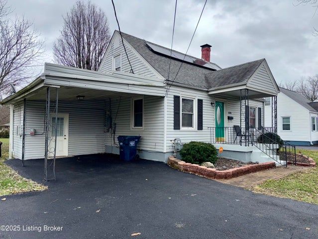 A light-colored house with a carport, driveway, and solar panels on the roof under a cloudy sky.