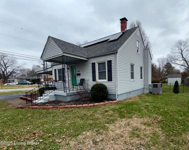 A light gray house with a black roof and solar panels, featuring a green door and brick-lined flower beds.