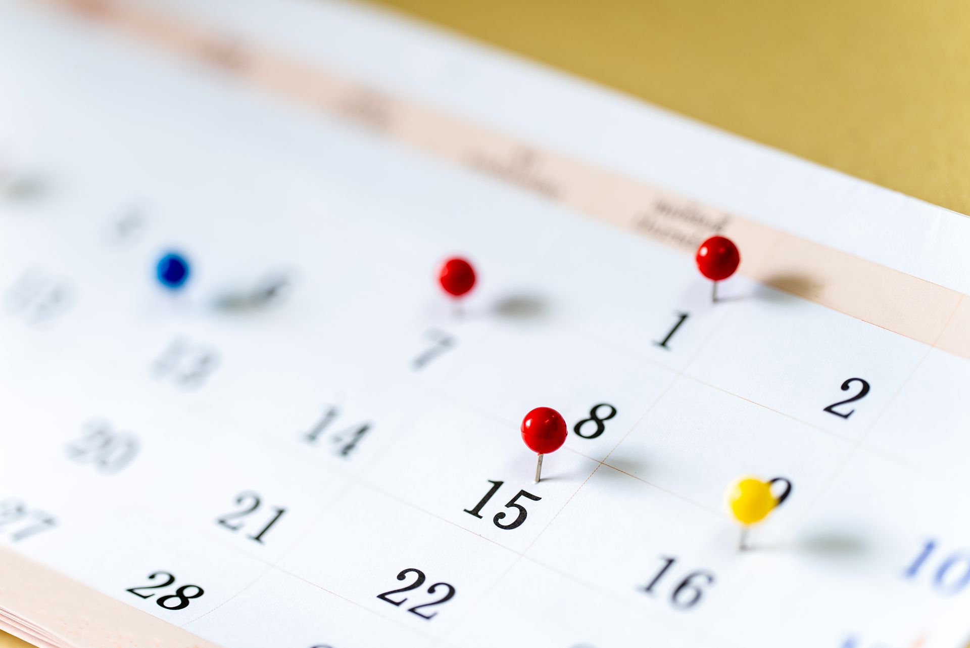 Close-up of a calendar page with colorful pushpins marking dates