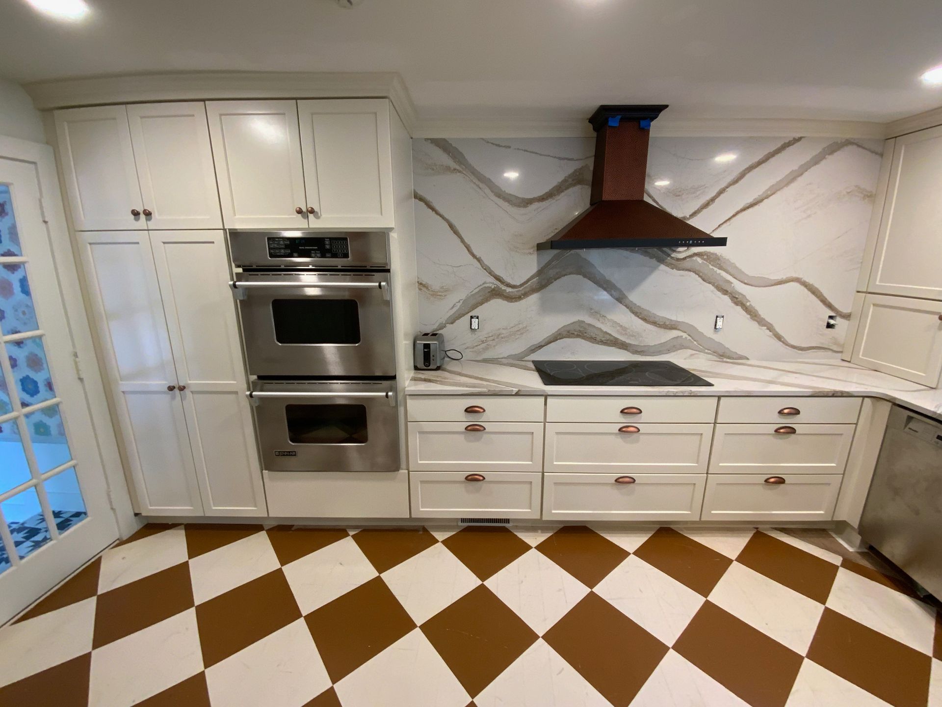 A kitchen with white cabinets , stainless steel appliances , and a checkered floor.