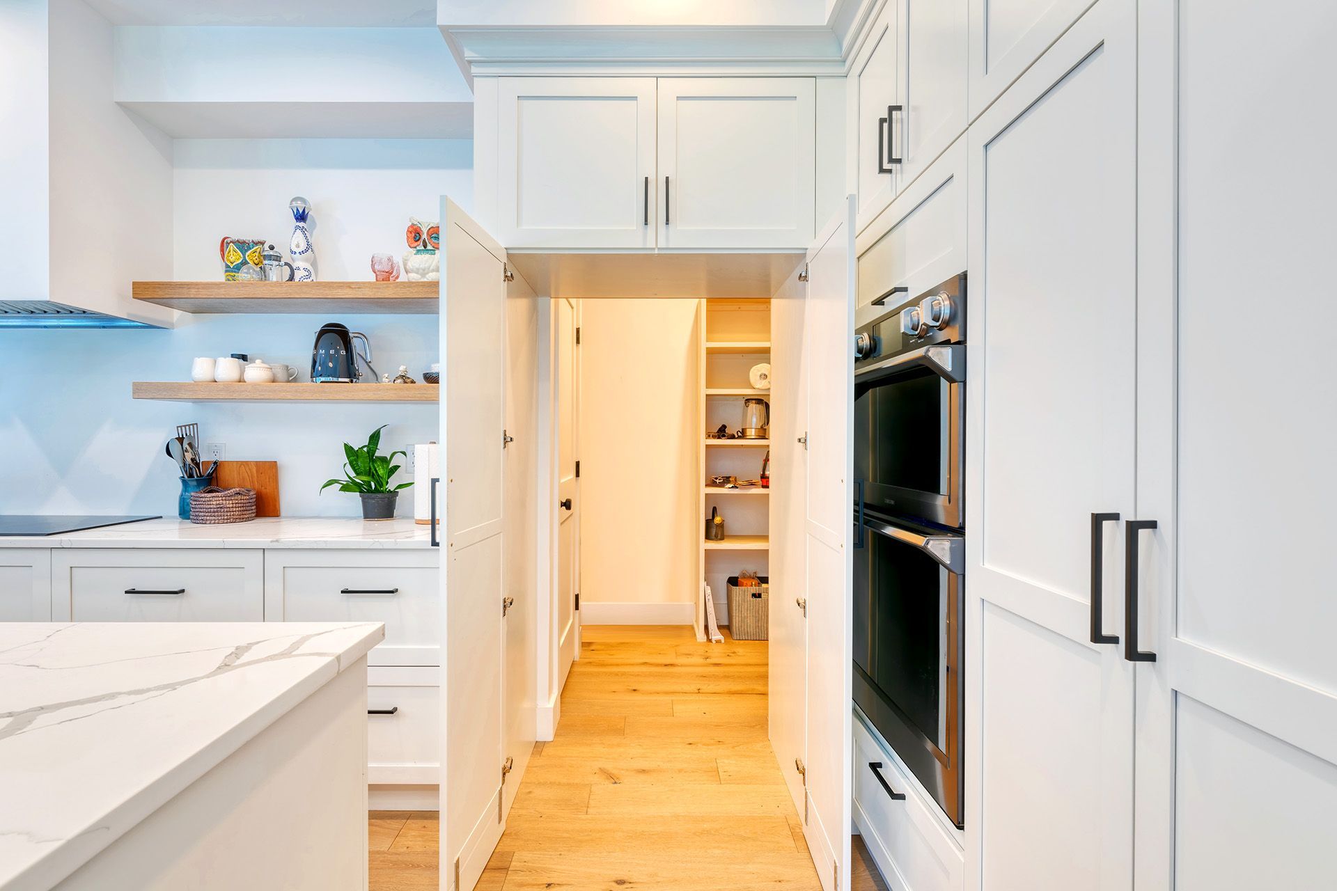 A kitchen with white cabinets and wooden floors and a pantry.