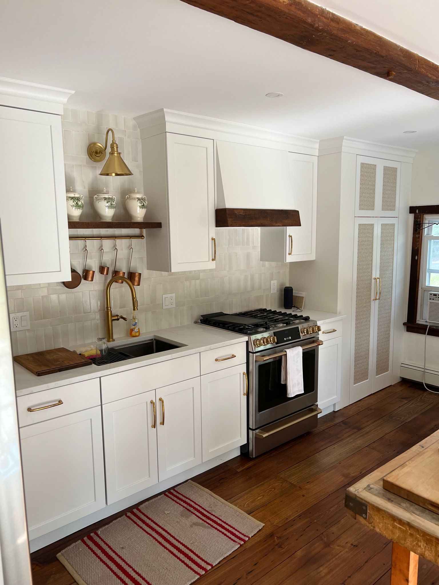Rustic kitchen with white cabinets, brass accents, wooden countertop, oven, and farmhouse sink. Warm lighting and wood flooring enhance coziness.