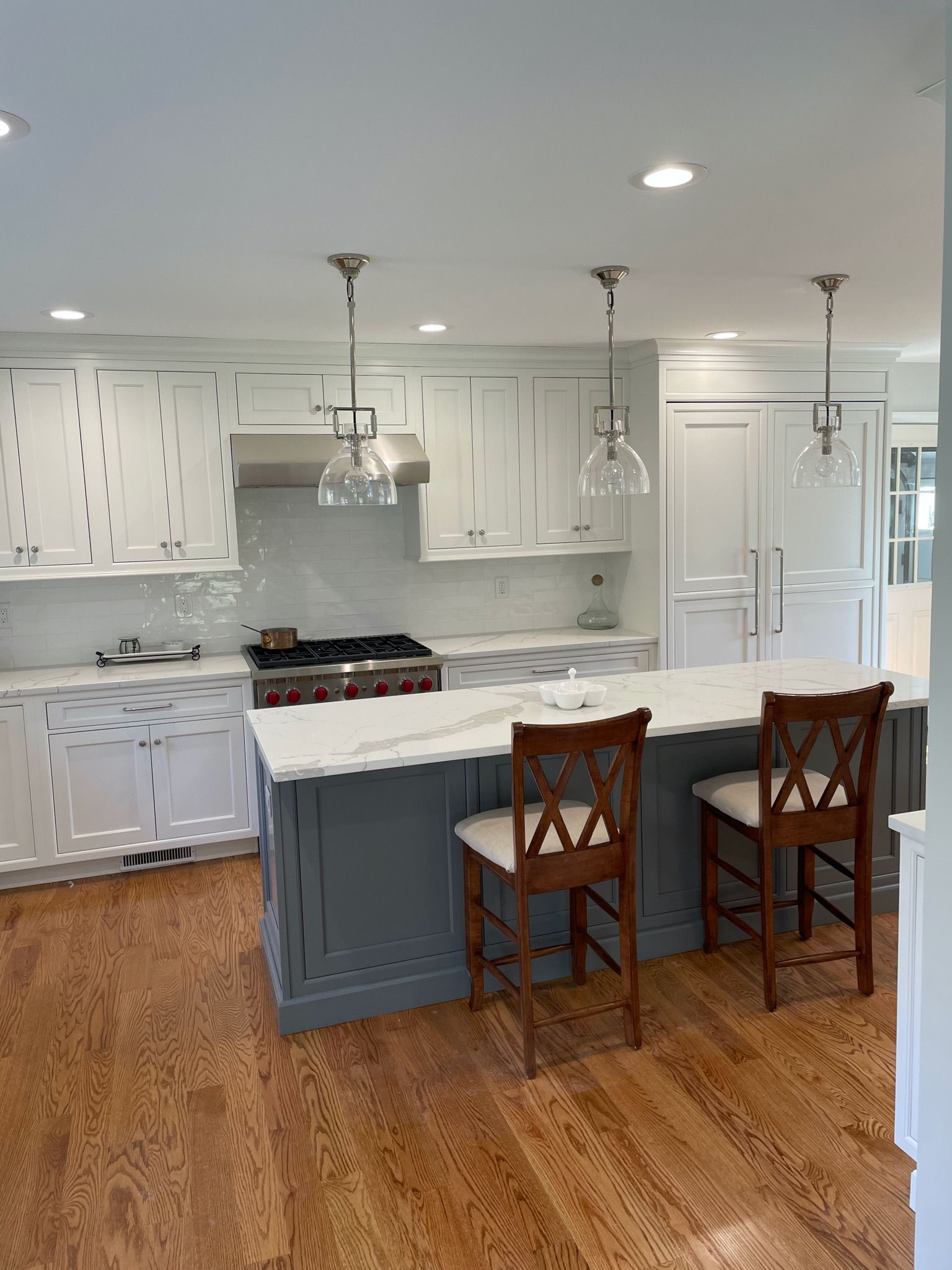 A kitchen with white cabinets , a large island , a stove and two chairs.