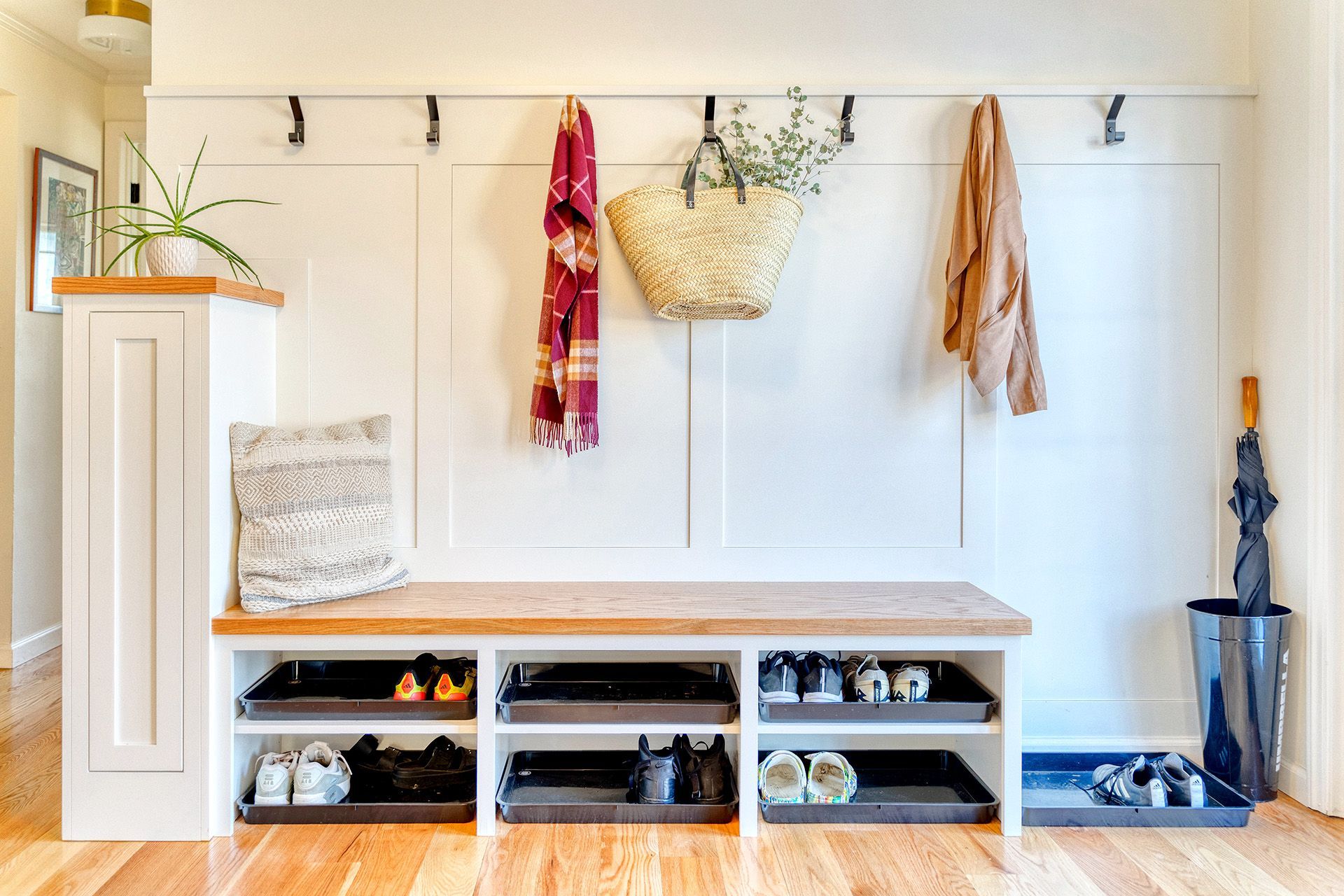 A hallway with a bench , shelves , hooks and umbrella holder.