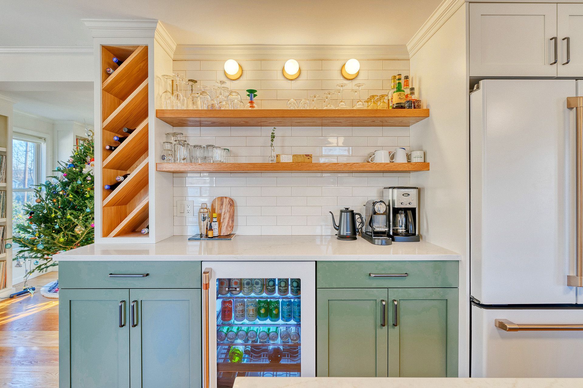 A kitchen with green cabinets , a refrigerator , a coffee maker , and a wine rack.