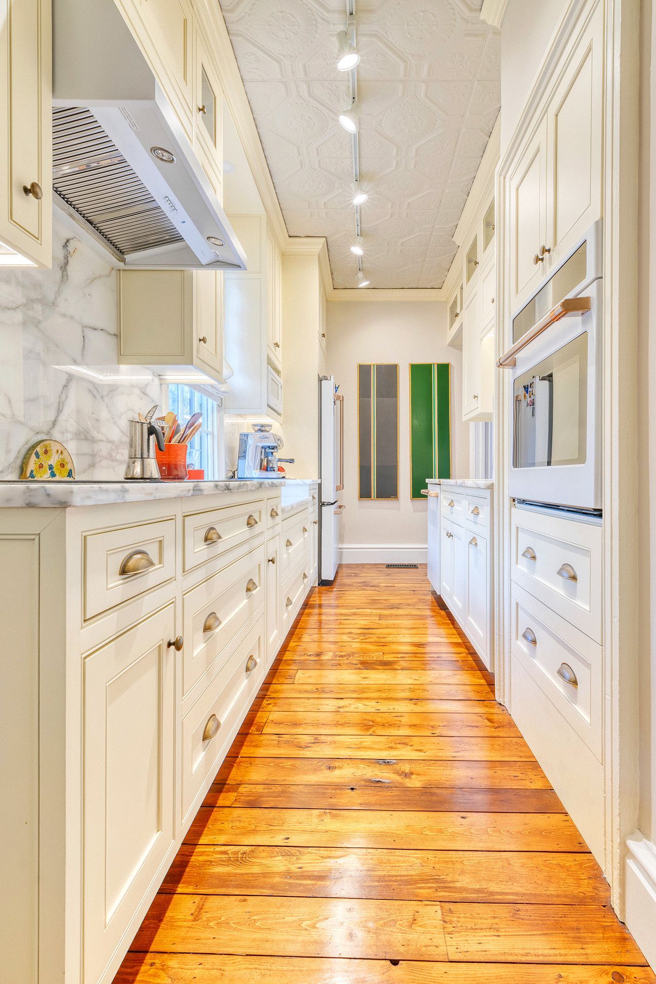 A long kitchen with white cabinets and wooden floors.