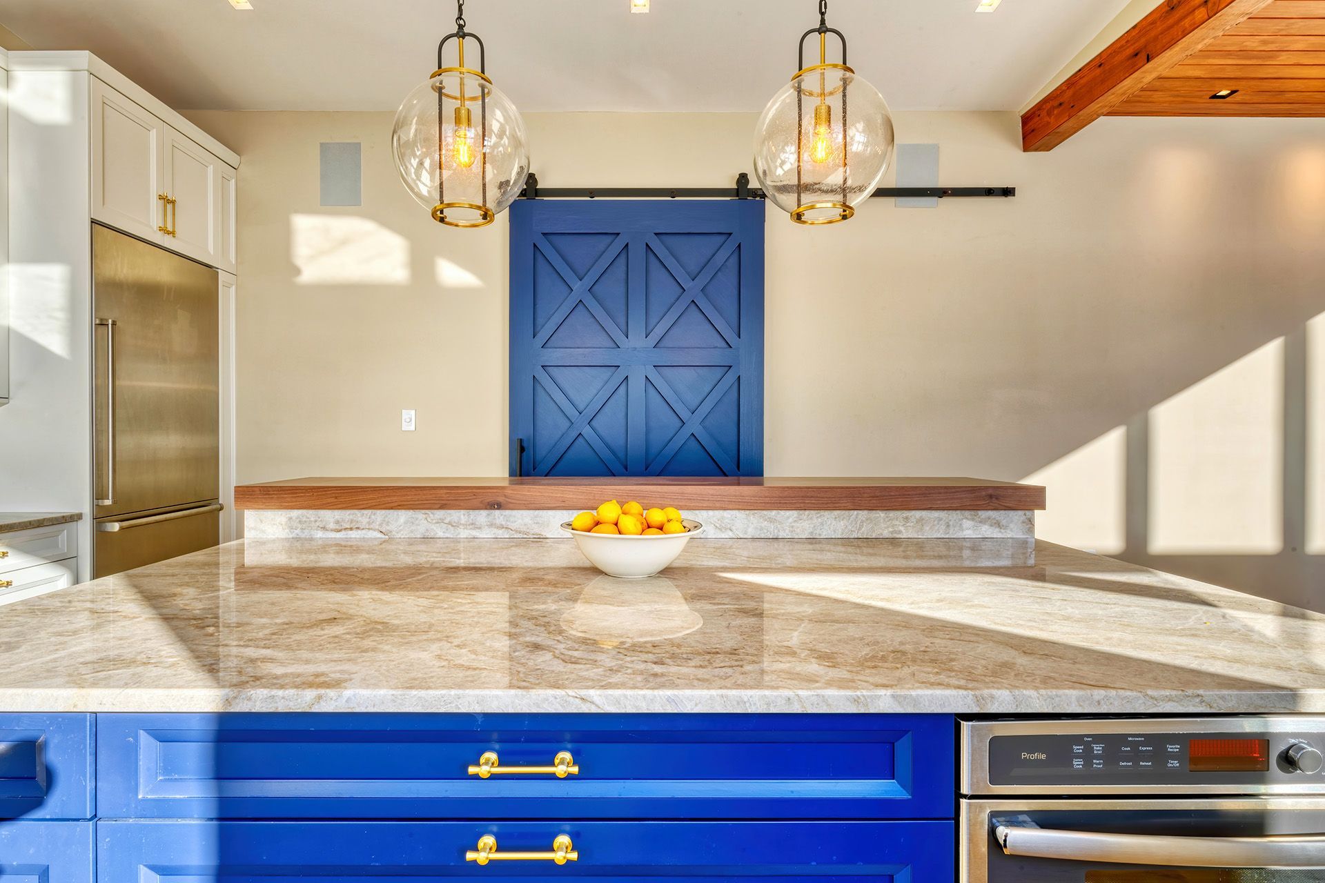 Dining room with a wooden table, blue chairs, and a connected kitchen. Sunlight streams in through the windows, illuminating the space.