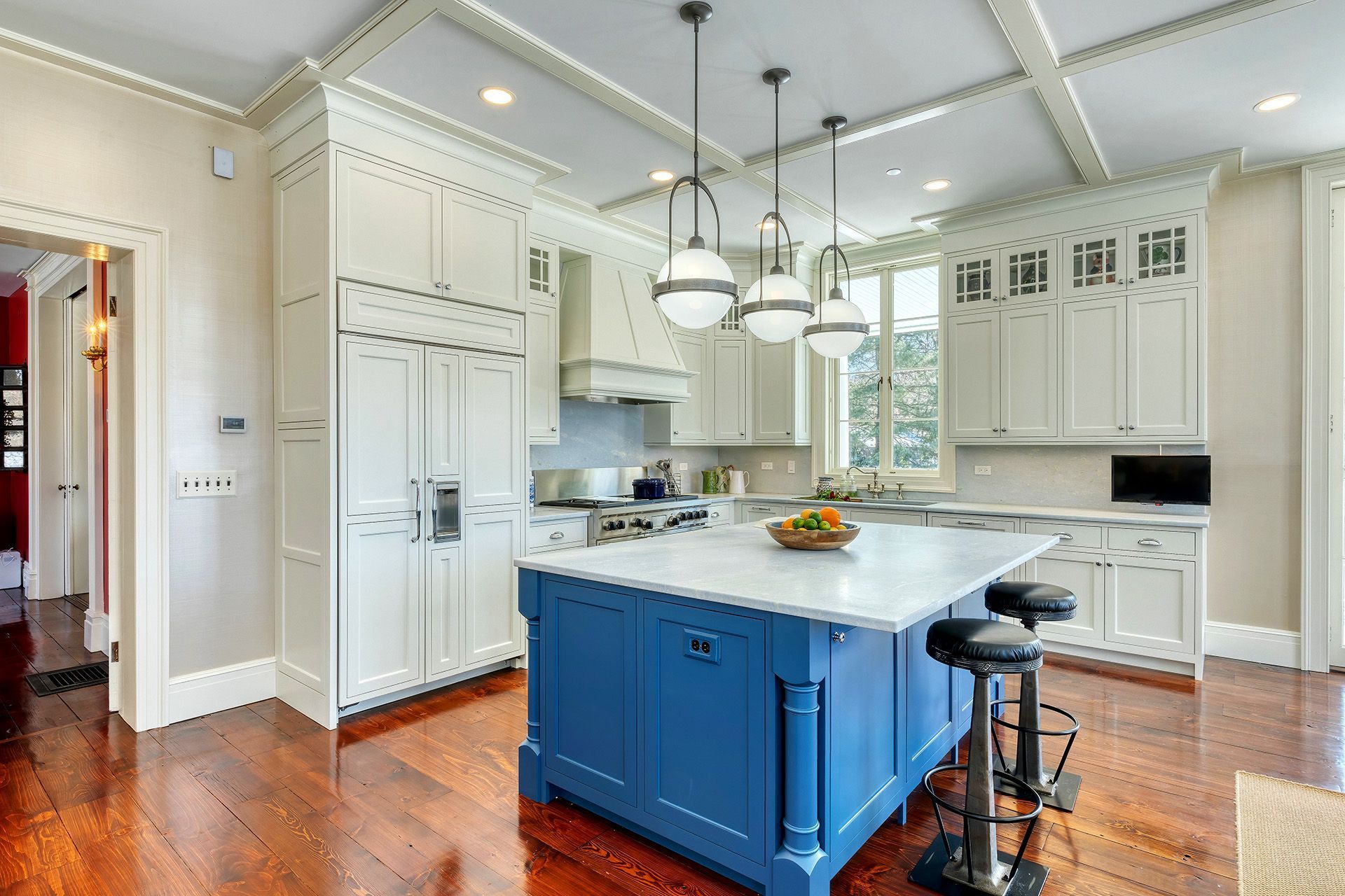 Spacious kitchen with two blue islands, white cabinetry, a long wooden dining table, and a coffered ceiling.
