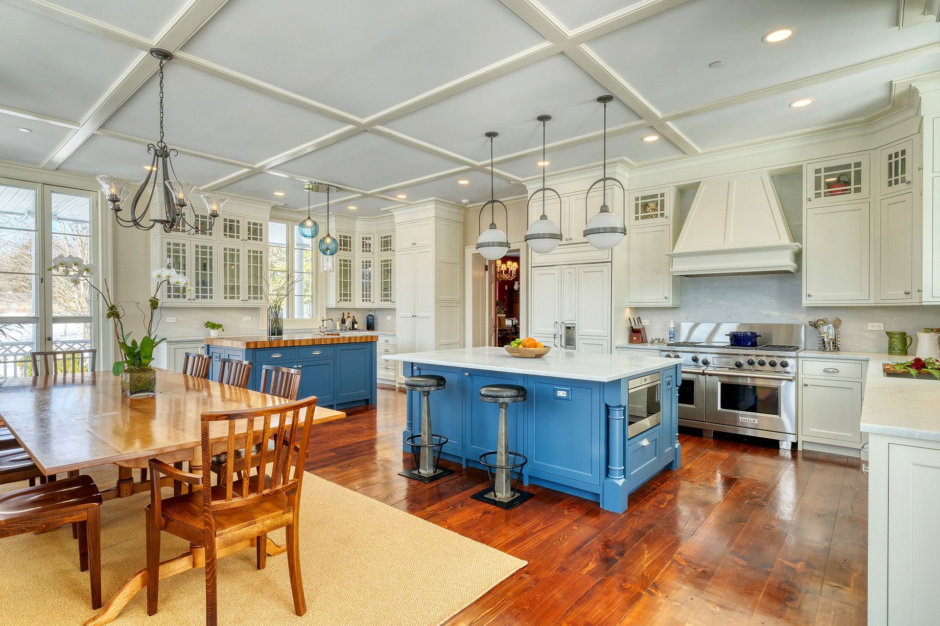 Spacious kitchen with blue islands, white cabinetry, and a long wooden dining table on hardwood floors.