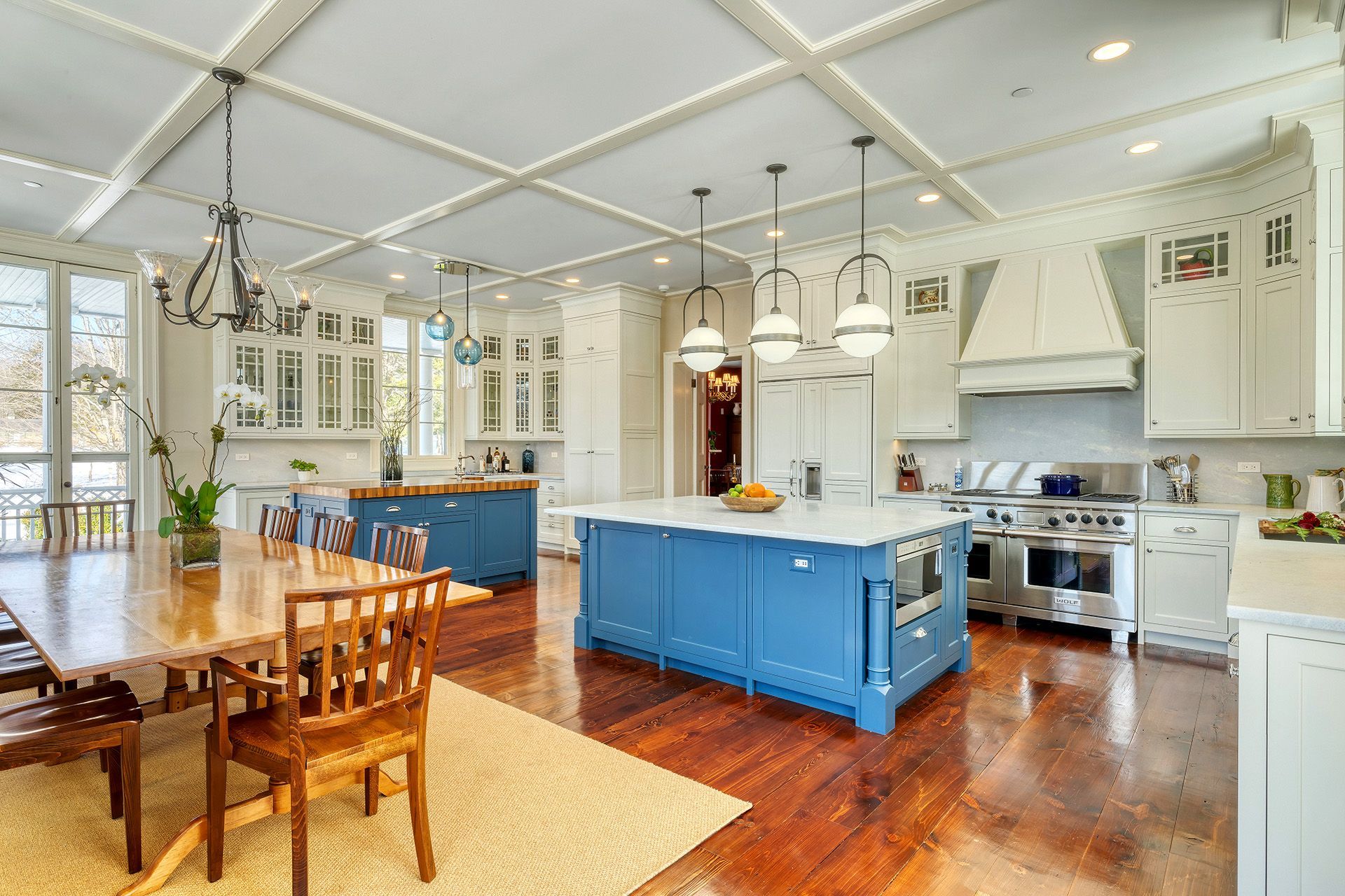 Spacious, light-filled kitchen with blue island, white cabinets, wooden dining table and wood floors.