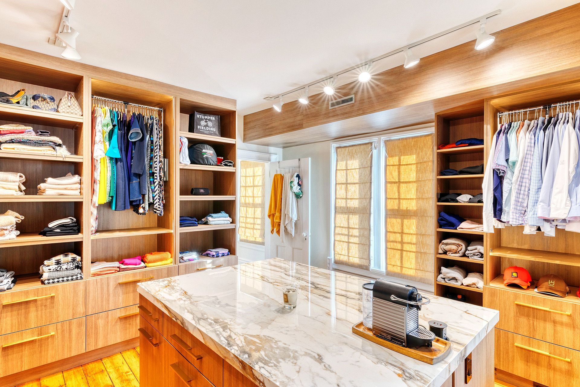 A walk in closet with lots of clothes and a large island in the middle.