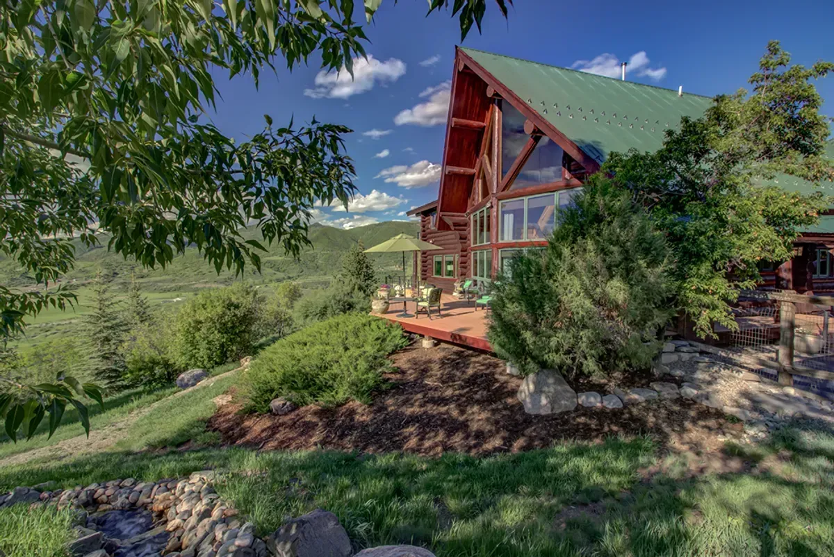 A large log cabin is sitting on top of a hill surrounded by trees.