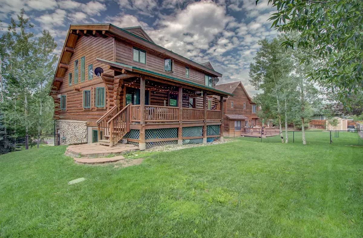 A large log cabin with a large porch in the middle of a lush green field.