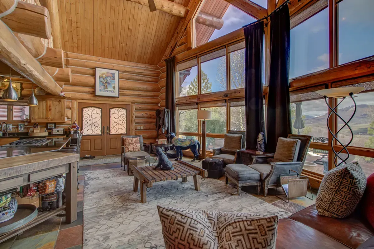 A living room in a log cabin with lots of windows and furniture.