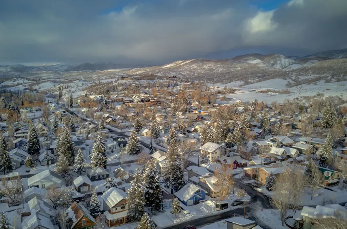 An aerial view of a snowy residential area with mountains in the background.