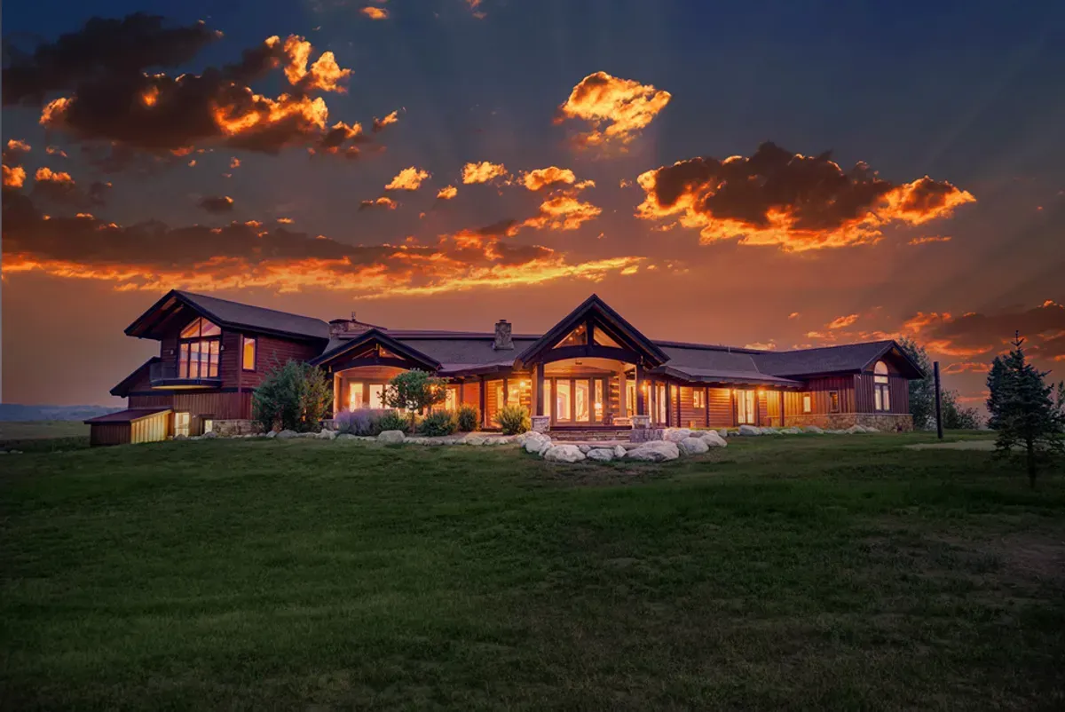 A large house is sitting on top of a lush green field at sunset.